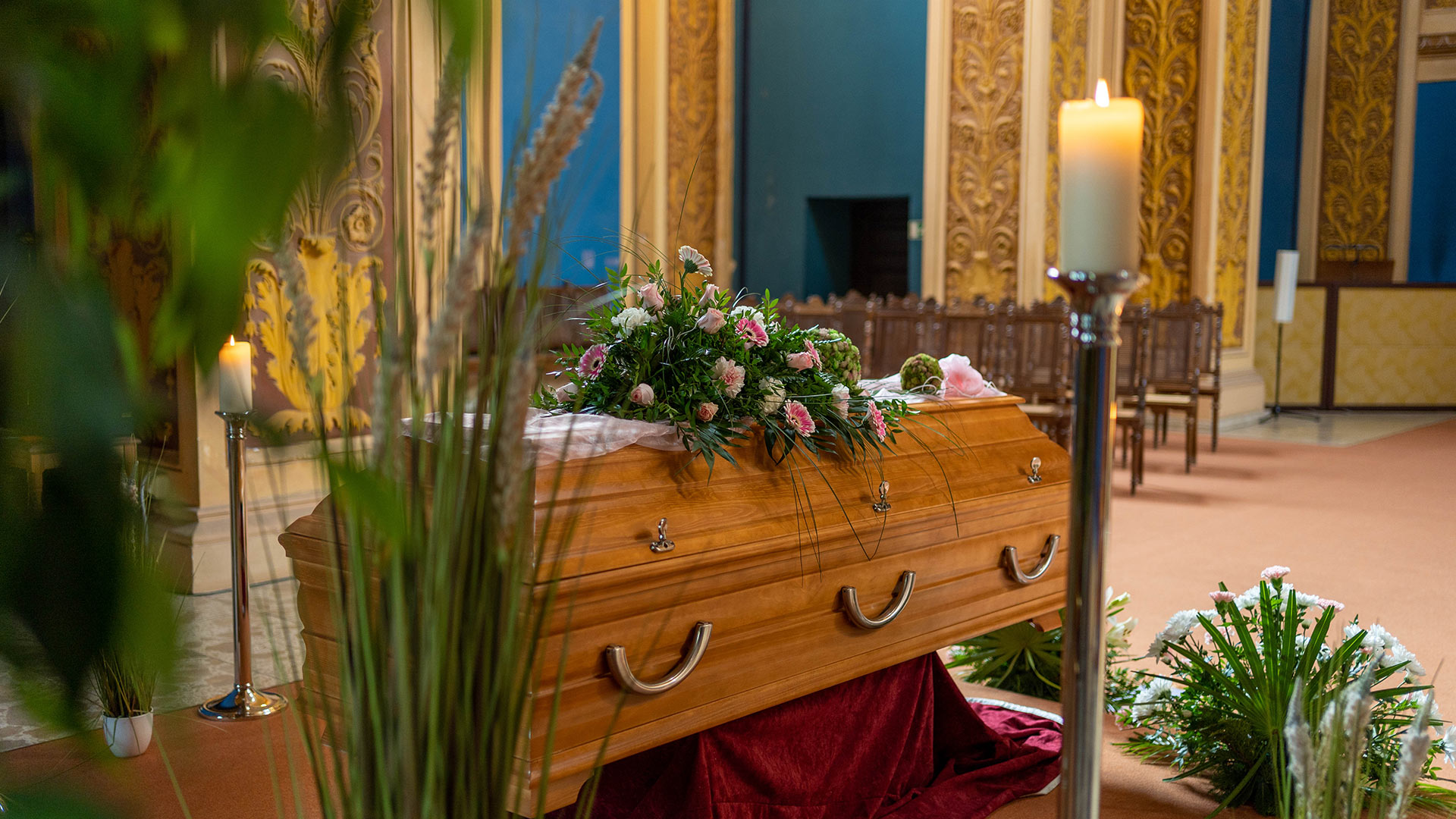 Ein hölzerner Sarg mit Blumenschmuck steht in einer festlich geschmückten Halle