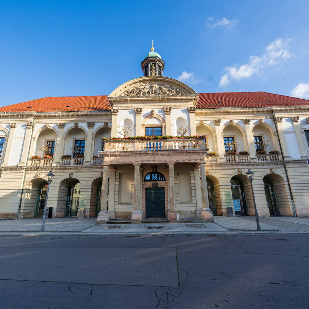 Ein historisches Gebäude mit rotem Dach, Rundbogenfenstern und Säulen im Sonnenlicht