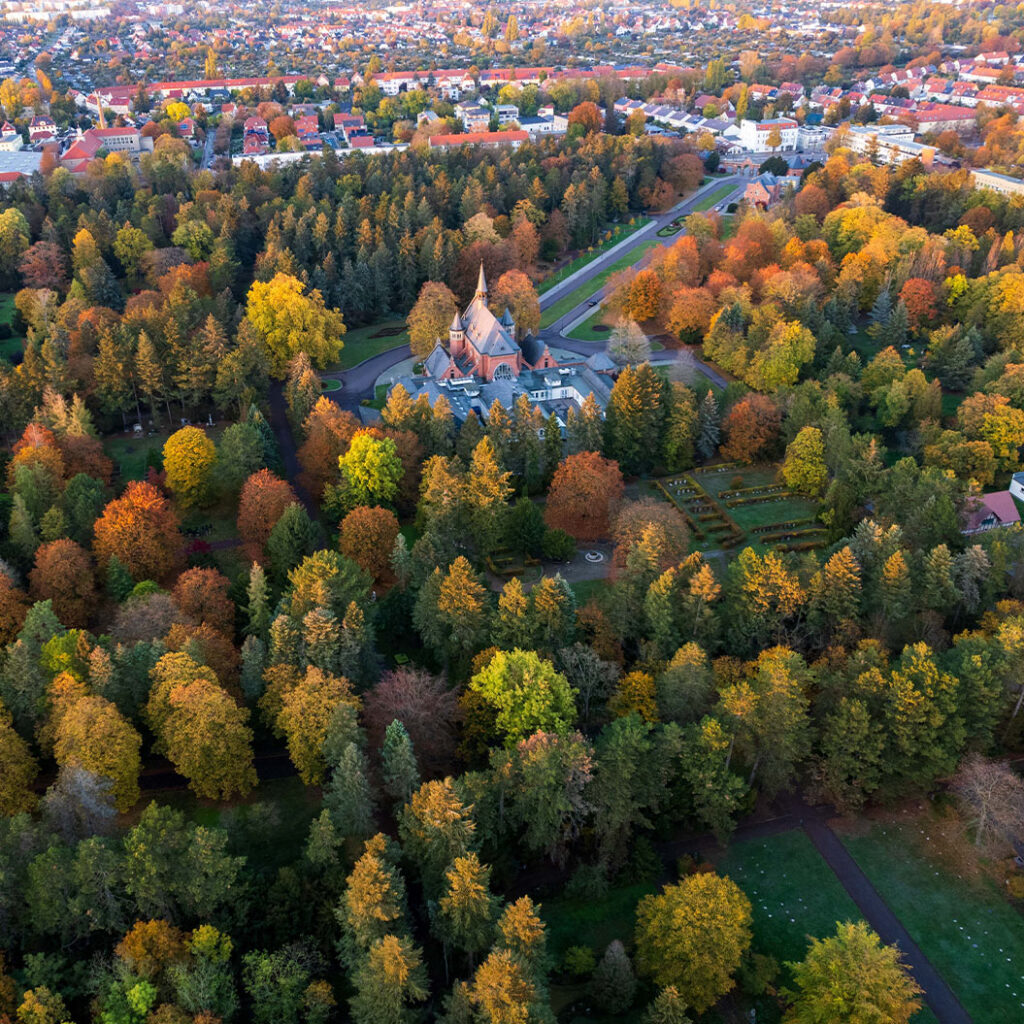 Luftaufnahme eines Parks mit herbstlich bunten Bäumen und einer Kirche in der Mitte