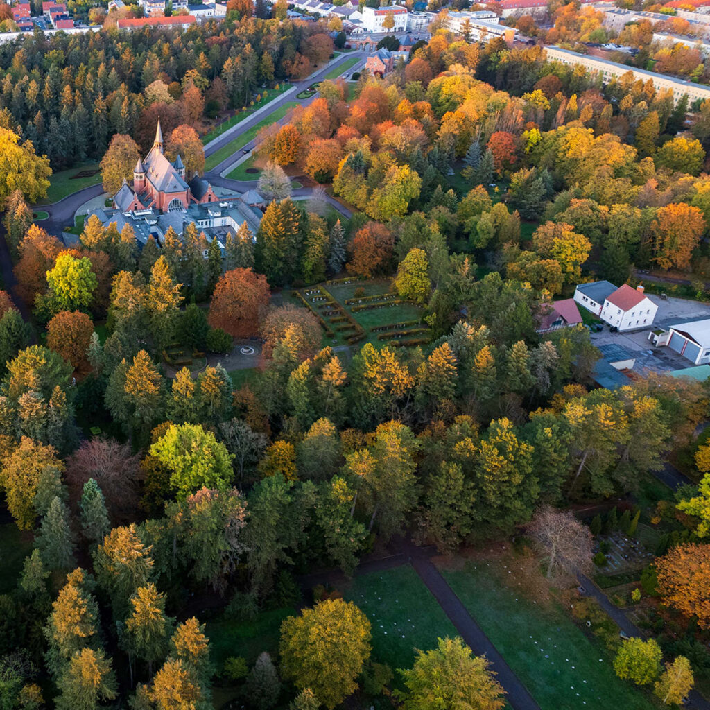 Luftaufnahme eines herbstlichen Parks mit einer Kirche, bunten Bäumen und Gärten