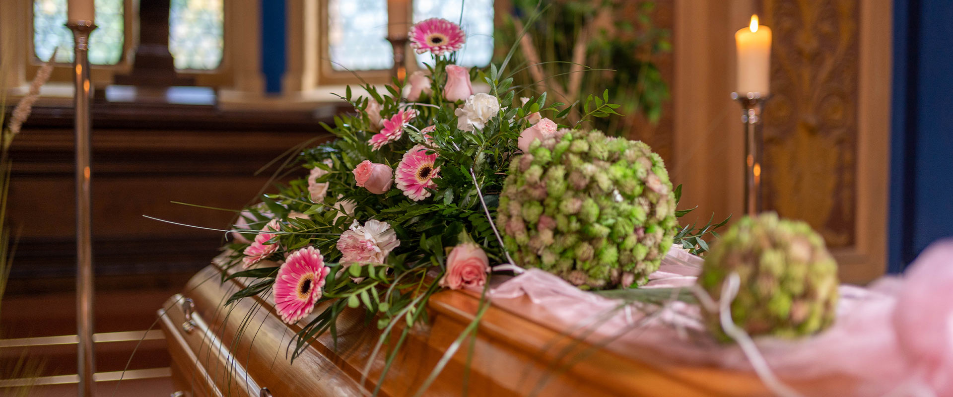 Holzsarg mit rosa und grünen Blumenarrangements in einer hell erleuchteten Kapelle
