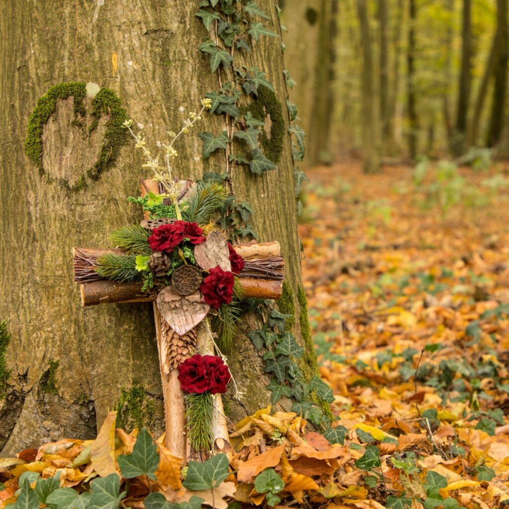 Ruhestätte in einem Friedwald mit einem dekorierten Holzkreuz am Baum