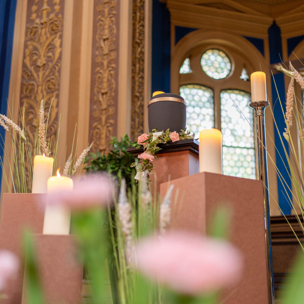 Eine Urne steht dekorativ umgeben von Kerzen und Blumen in einem festlichen Raum